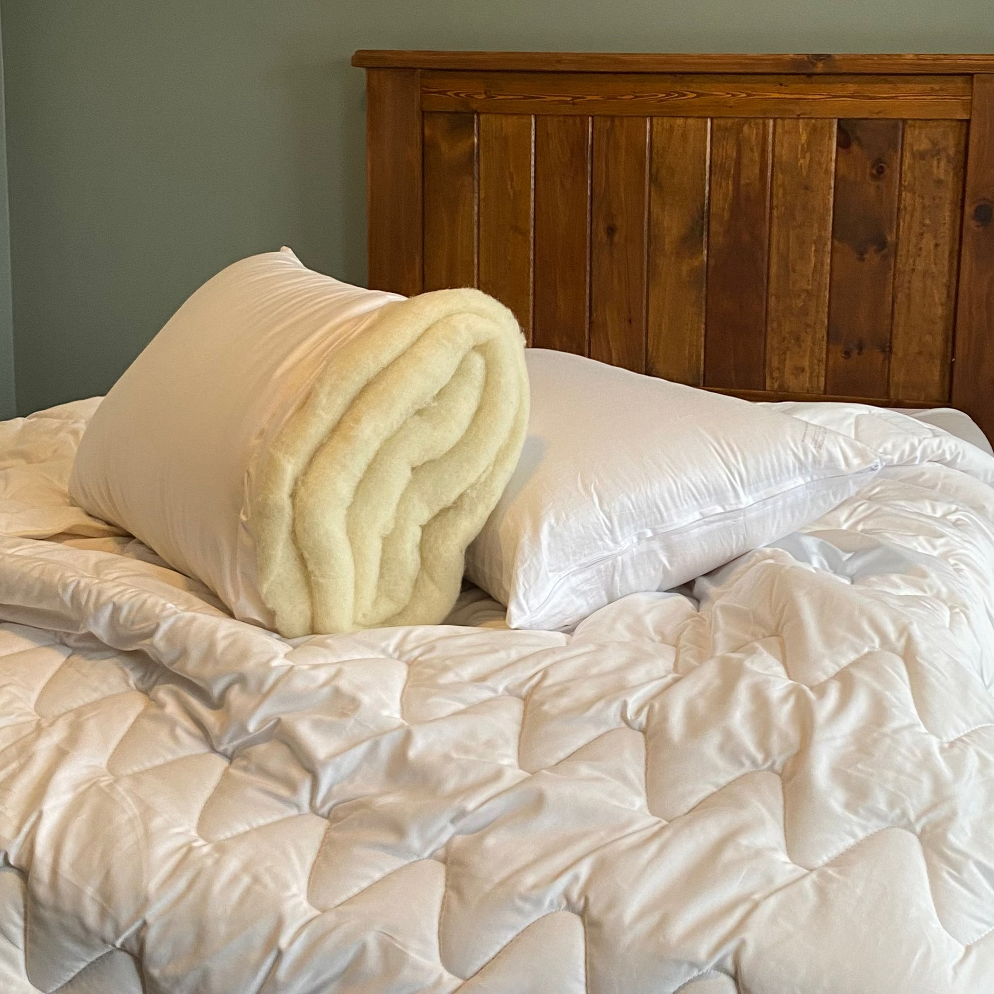 Bedroom with wooden headboard, white bedding, and pillow opened up to show the wool filling inside.