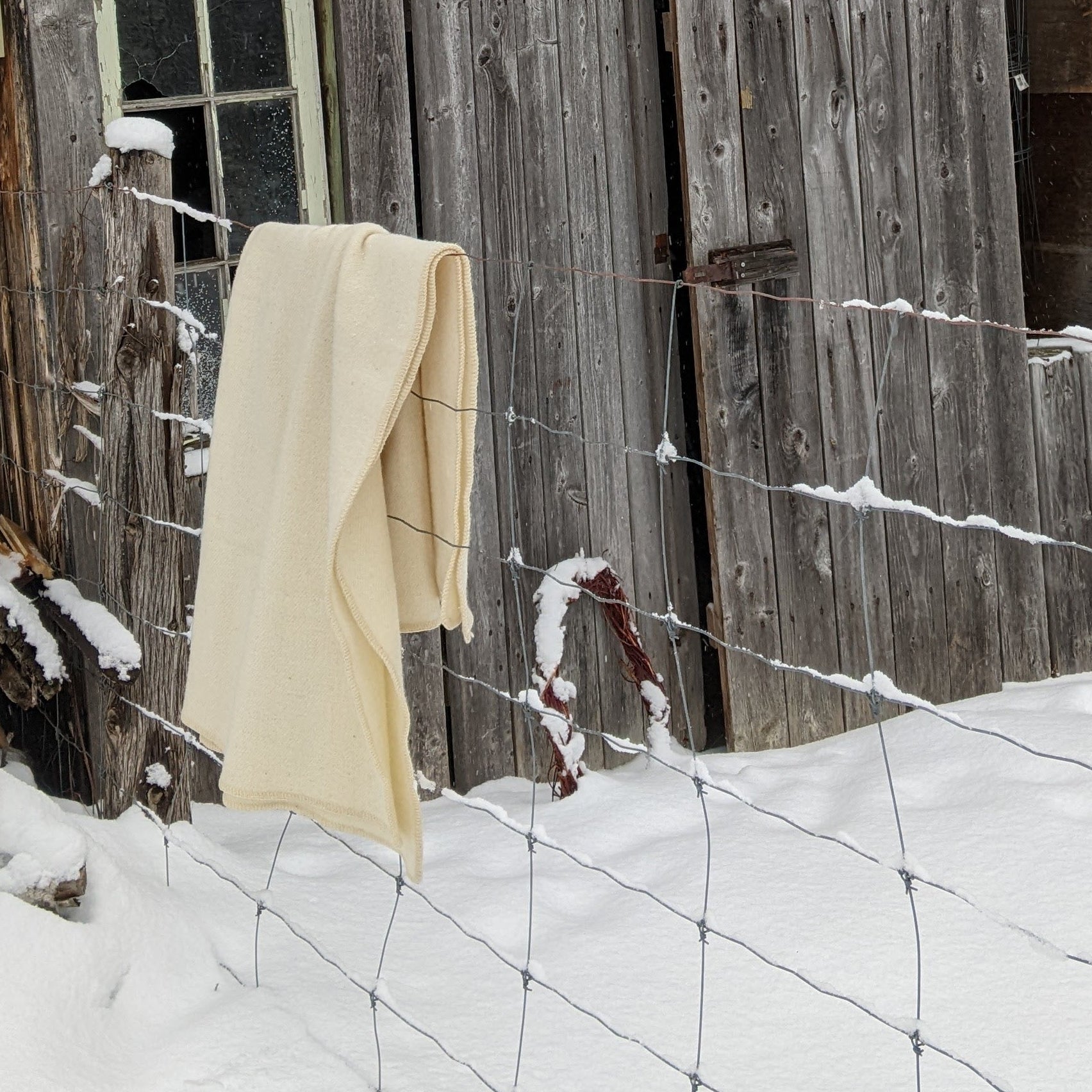 Old wooden barn with a white blanket hanging on a hook in a snowy landscape